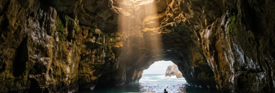 Grotte marine portugaise baignée d'une lumière dorée traversant une ouverture circulaire dans la roche calcaire, avec une petite embarcation en contrebas